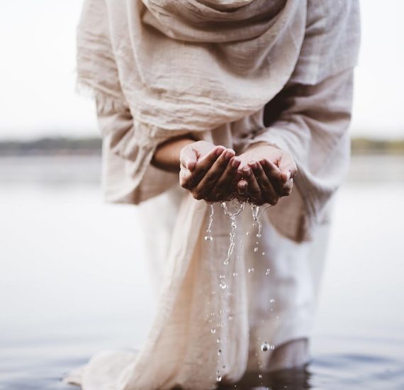 A closeup shot of a female wearing a biblical robe holding water with her palms